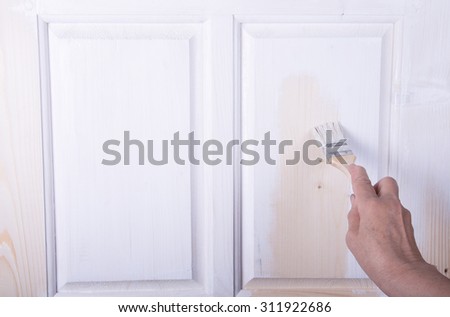 Hand of an elderly woman with a paint brush with white paint door. Selected focus