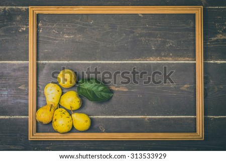 Yellow seasonal pears with leaf in wooden frame on the background of old boards. Toned.