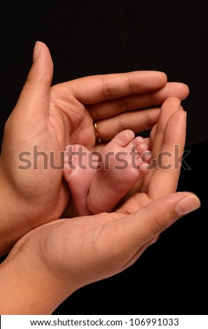 A loving and caring mother is holding the feet of her first new born baby girl and gently enclosing her soft and warm fingers and palms around the tiny feet and toes