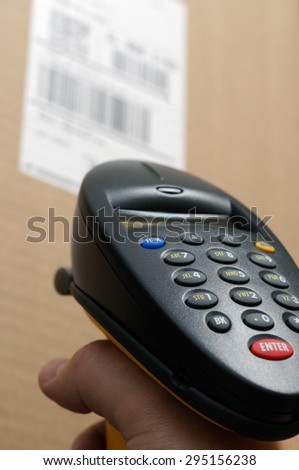 Picture of person's hand holding a barcode scanner reader up to a brown box with a UPC bar code label.