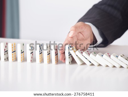 Businessman in formal suit stopping falling dominoes - concept for strategy and problem solving