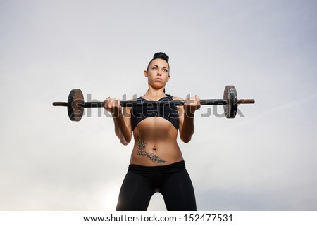 The girl with a sports figure does exercises with barbell