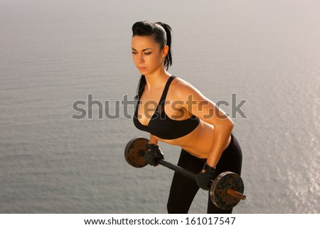 The girl with a sports figure does exercises with barbell