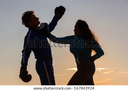 A woman and men is silhouetted in the colorful sky with boxing gloves