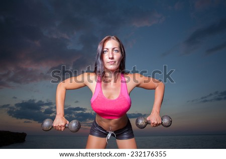 The girl with a sports figure does exercises with dumbbells