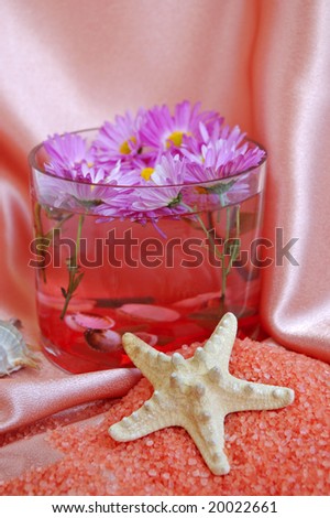 A bright pink spa and body care background. Salt and flower floating in glass bowl.
