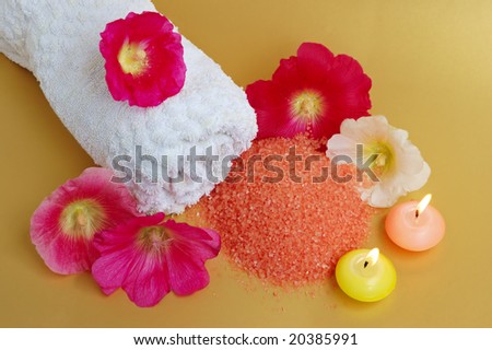 Still life of beauty treatment items with aromatherapy candles, towel, salt and flowers.