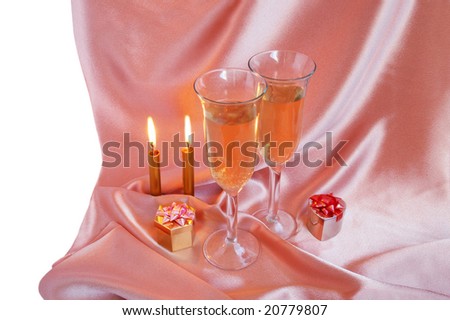 Pair of champagne flutes with candles and gift box on silk background
