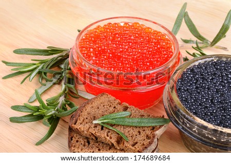 Red and black caviar in glass cans with bread on wooden background