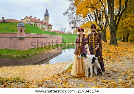 Nesvizh, Belarus - October 12: Couple in costumes of Grand Duchy of Lithuania with Russian borzoi dog represents everyday life of the nobility with Nesvizh Castle in background on October 12, 2013.