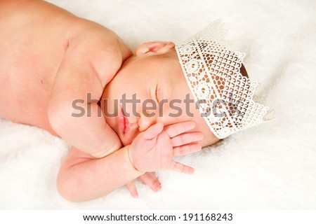 Newborn 12 day old baby boy lying on his back relaxing under a wrap cloth. Portrait old newborn baby boy wearing a gold crown.
