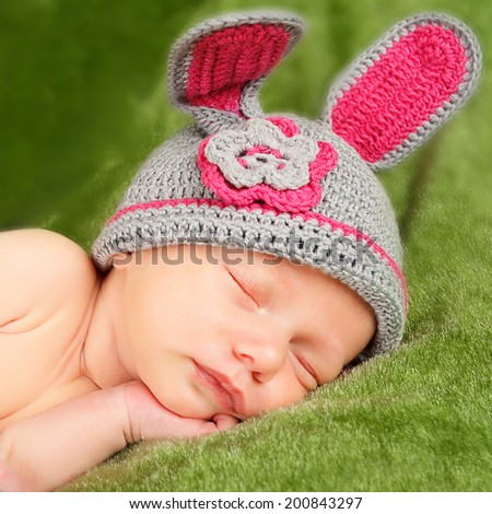 Eight day old smiling newborn baby wearing bunny ears and a bunny tail diaper cover. The baby is sleeping on his stomach.