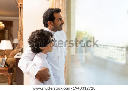 Arabian father embracing son at home  looking at the window 