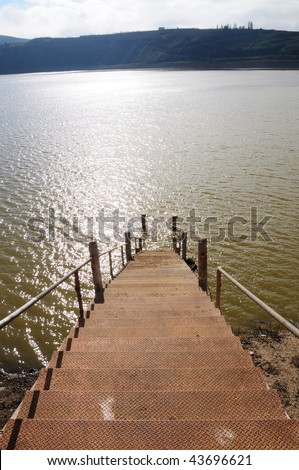 Ladder with metal rungs. The descent to the water. Sun Spots on the surface of water.