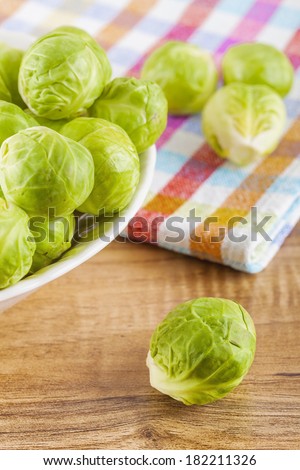 Overhead shot of brussels sprouts in a ceramic bowl and on a wooden table with a cloth rag/Brussels sprouts served on a table
