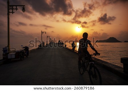 Silhouetted unidentified man riding a bike on jetty at Ao Manao bay in Prachuap Khiri Khan, Thailand