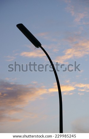 A single curved street lamp stands in front of a beautiful sunset / Lantern before sunset