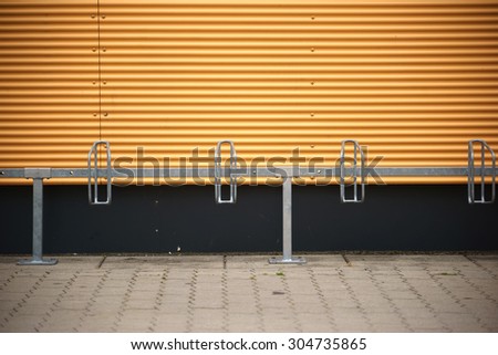A number of bike racks mounted in front of a distinctively colored corrugated iron facade / Bicycle stands in front of corrugated iron wall