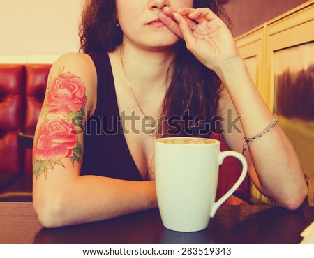 young beautiful hipster tattooed  woman with red curly hair at the bar with cup of coffee. Vintage style picture