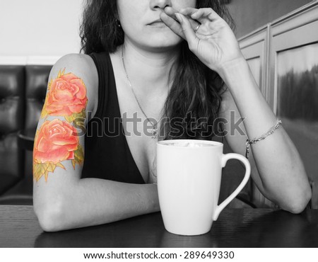 young beautiful hipster tattooed woman with red curly hair at the bar with cup of coffee. Black and white picture with colored tattoo. Concept background