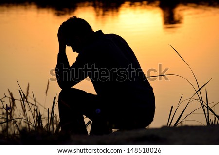 depressed man sitting against the light reflected in the water