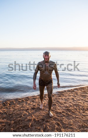 DEAD SEA RESORT, JORDAN - APR 30, 2014: Unidentified man in Dead Sea mud poses for the camera. The mud of Dead Sea is being used with  the therapy purposses for the people with skin problems
