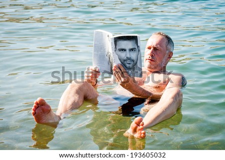 DEAD SEA RESORT, JORDAN - MAY 1, 2014: Unidentified man reads a book laying on the water surface of the Dead Sea. Dead Sea water is used for medical purposes for the people with skin problems