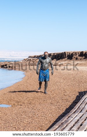 DEAD SEA RESORT, JORDAN - APR 30, 2014: Unidentified man in a Dead Sea mud walks on the beach. Dead Sea mud posesses the medical qualities