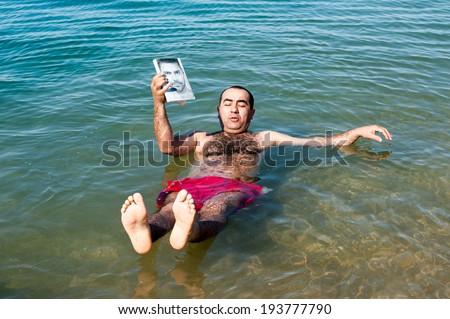 DEAD SEA RESORT, JORDAN - MAY 1, 2014: Unidentified man swims on the salty water of the Dead Sea. Dead Sea water is used for medical purposes for the people with skin problems