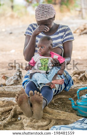 ACCRA, GHANA - MARCH 6, 2012: Unidentified Ghanaian woman and her little baby sit near the tree in the street in Ghana. People of Ghana suffer of poverty due to the unstable economic situation