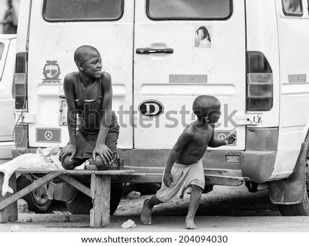 ACCARA, GHANA - MAR 2, 2012: Unidentified Ghanaian boys sit near the a back of the car in the street in black and white. People of Ghana suffer of poverty due to the unstable economical situation