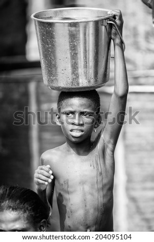 ACCARA, GHANA - MAR 2, 2012: Unidentified Ghanaian boy with a bucket of water in the street  in black and white. Children of Ghana suffer of poverty due to the unstable economical situation