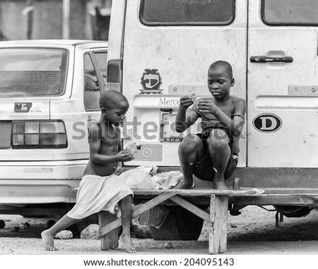 ACCARA, GHANA - MAR 2, 2012: Unidentified Ghanaian boys sit near the a back of the car in the street in black and white. People of Ghana suffer of poverty due to the unstable economical situation