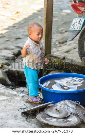 LAO CHAI VILLAGE, VIETNAM - SEP 22, 2014: Unidentified Hmong little boy helps his mother to wash the dishes in Lao Chai. Hmong is on of the minority eethnic group in Vietnam