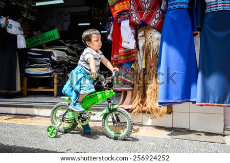 OTAVALO, ECUADOR - JAN 3, 2015: Unidentified Ecuadorian little boy on bike at the Otavalo Market. 71,9% of Ecuadorian people belong to the Mestizo ethnic group