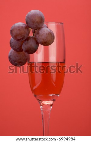 A glass of rose wine with grapes against a plain background.