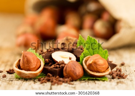 hazelnut with chocolate bars and green leaves on old wooden background