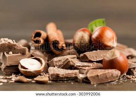 Broken chocolate bar, hazelnut and cinnamon on wooden background, close-up