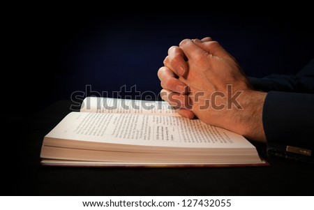 Clasped hands on a bible while praying to God.