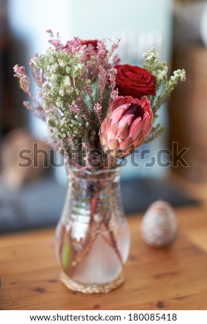 Narrow focus flowers in a glass jug on a wooden table.