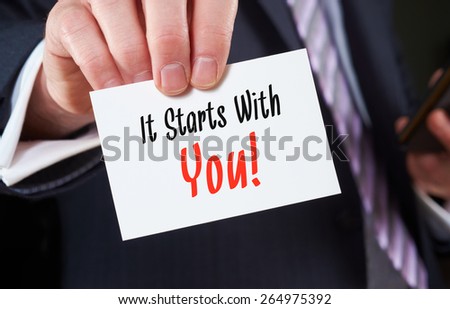 A businessman holding a business card with the words, It starts with You.