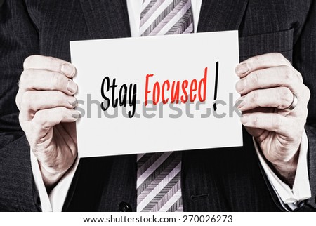 A businessman holding a card with the words, Stay Focused, written on it