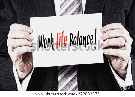 A businessman holding a card with the words, Work Life Balance, written on it.
