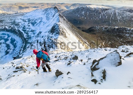 A hiker descending Helvellyn towards Striding Edge and Red Tarn in the Lake District, UK.
