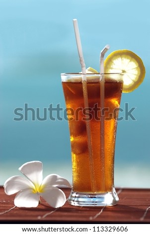glass of iced tea by the sea Iced tea with lemon and sea background. Located on a bamboo mat and a frangipani flower