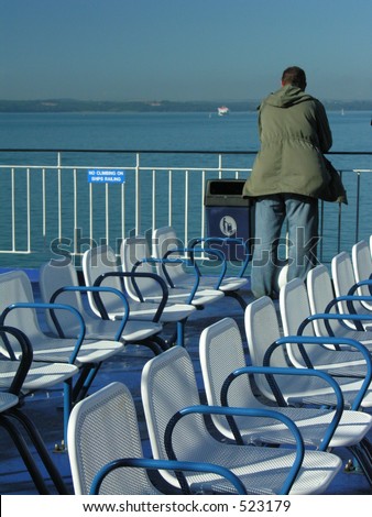A man looking out to sea with a row of empty seats in the foreground.  Taken on a ferry deck.