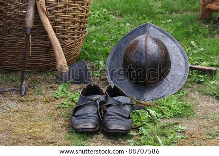 Still life objects at a medieval reenactment display. Features tools including an axe and a fighting hat and shoes.