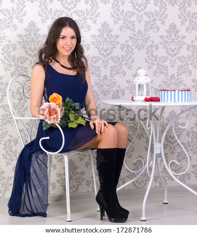 girl in a blue dress sitting at a table with flowers in hand