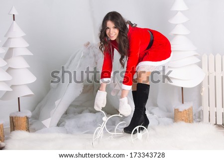 happy girl dressed as Santa Claus wants to sit on a little bike