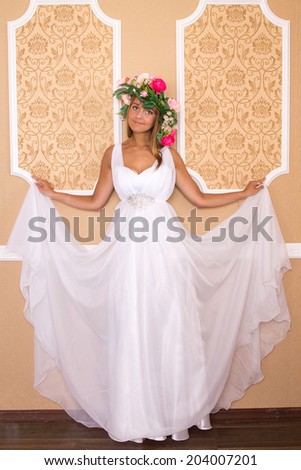 girl in white dress with wreath on his head on background of beige walls